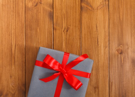 Present for any holiday concept. Gift box wrapped in gray paper, top view with copy space on wood table surface background. Package with red satin ribbon bow for christmas, valentine day or birthdayの写真素材