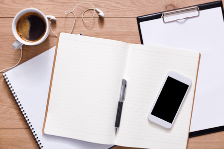 Notepad, diary, mobile phone and espresso coffee. Office or student's devices on modern wooden desk. Working table top view. Education or job background with copy space on paper sheetの写真素材