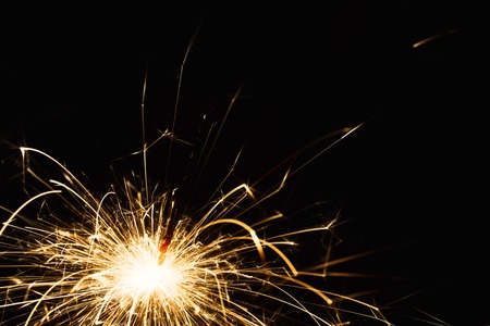 New year party burning sparkler closeup on black background. Glowing holiday sparkling hand fireworks, shining fire flame. Christmas light.の写真素材