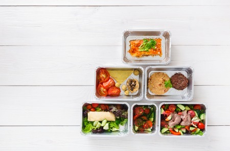 Healthy food delivery. Take away of natural organic fitness dishes for diet. Daily ratio nutrition pyramid meals in foil boxes on white wood. Top view, flat lay, copy space on wooden backgroundの写真素材