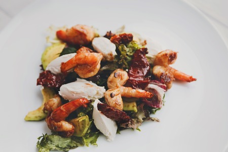Restaurant food. Traditional italian seafood salad with shrimps and mozzarella on white round plate. Diet and healthy meals closeup, filteredの写真素材