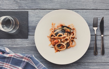 Restaurant food. Traditional italian seafood tomato pasta with calamari rings and mussels on white round plate. Diet and healthy meals, top view of served table, filtered imageの写真素材
