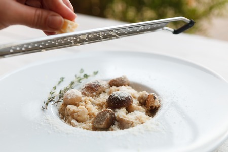 Chef grating parmesan cheese on wild mushrooms porcini risotto with rosemary. Traditional italian cuisine dish. Restaurant food closeup. Forest fungus with rice. Shallow DOF, selective focusの写真素材