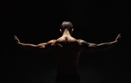 Unrecognizable man bodybuilder shows strong hands and neck muscles, athletic trapezius. Low key, studio shot on black background.の写真素材