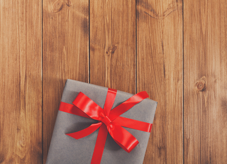 Present for any holiday concept. Gift box, top view with copy space on wood table surface background. Package with red satin ribbon bow for christmas, valentine day or birthdayの写真素材