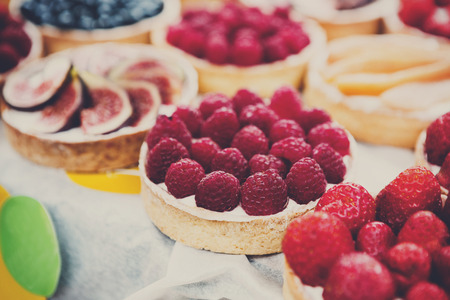 Fruit and berry tarts dessert tray assorted outdoors. Closeup of beautiful delicious pastry sweets with fresh natural raspberries and figs. French Bakery catering. Filtered, shallow depth of fieldの写真素材