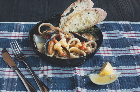 Seafood Stew in Saucepan. Authentic italian restaurant cuisine, healthy delicatessen food. Oysters, shrimps, calamari in white cream sauce with bruschetta. Bowl closeup on served tableの写真素材