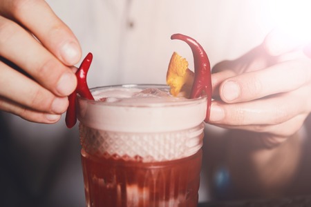 Barmans special - frothy exotic spicy alcohol cocktail with chili peppers and orange in restaurant at bar background. Glass on bar table, original and creative refreshing drink.の写真素材