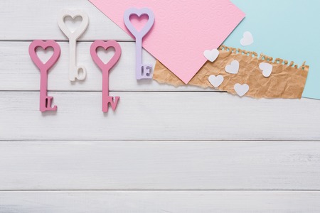 Key from love. Happy Valentines Day background with heart in keys form, greeting cards and paper letters, pastel pink and violet decorations, copy space on white wood planksの写真素材