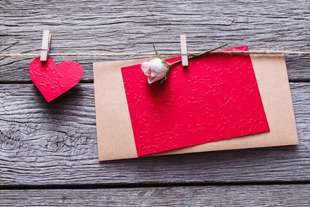Valentine background with red paper heart and empty greeting card on clothespins on rustic wood planks. Happy lovers day card mockup, copy spaceの写真素材