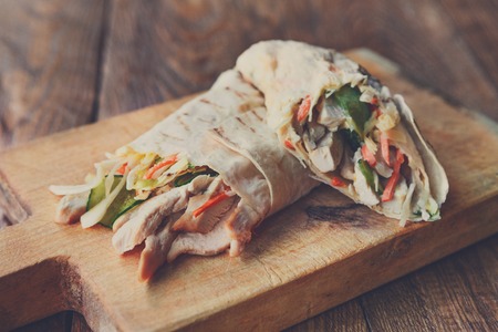 Mexican restaurant fast food - wrapped burritos with pork meat and vegetables closeup at wooden desk on table. Mexican burritos closeup.の写真素材