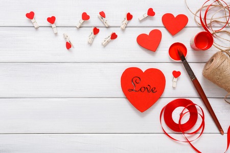 Valentines day, wedding or other holiday decorations, frame background. Handmade gift greeting card creating, painting red color, craft paper and diy tools on white wood. Above view, flat layの写真素材