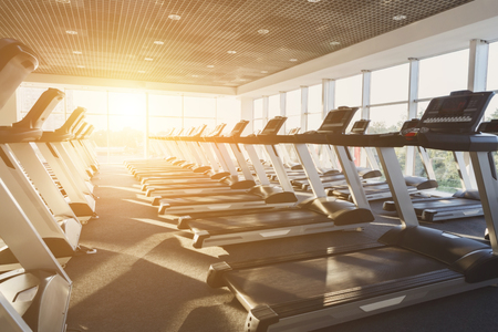 Modern gym interior with equipment. Fitness club with row of treadmills for fitness cardio training in evening backlight. Healthy lifestyle conceptの写真素材