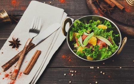 Vegan and vegetarian dish, fresh vegetable salad in copper bowl. Indian restaurant, lettuce and fruits mix with herbs, healthy meal, top view on wood background. Eastern local cuisine food.の写真素材
