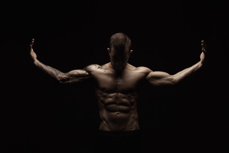 Strong athletic man. Handsome male fitness model showing naked torso, muscular body. Strong hands, chest and shoulder muscles and biceps. Studio shot on black background, low key. Bodybuilding conceptの写真素材