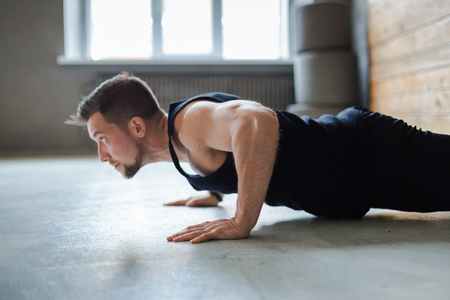 Young man workout in fitness club. Profile portrait of caucasian guy making plank or push ups exercise, training indoorsの写真素材