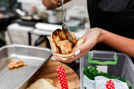 Female street vendor hands put ketchup sauce in taco outdoors. Mexican cuisine snacks, cooking fast food for commercial kitchen.の写真素材