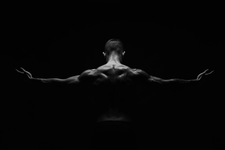 Unrecognizable man bodybuilder shows strong hands and neck muscles, athletic trapezius. Black and white, monochrome studio shot on black background.の写真素材