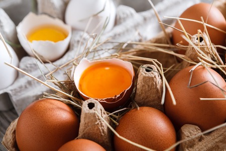 Eggs carton closeup, fresh natural healthy food background. Brown and white cracked eggs with bright yellow yolk. Organic farming concept.の写真素材