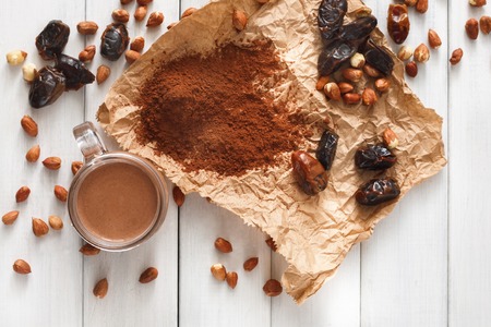 Detox cleanse drink background. Chocolate smoothie ingredients. Natural healthy juice in glass jar for diet or fasting day. Cocoa powder, nuts, date fruit mix on white wood, top viewの写真素材