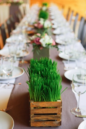 Beautifully organized event - served festive table ready for guests, decorated with grass and flowers. Event in restaurant outdoors. Banquet, wedding decor, celebration. Vertical orientationの写真素材