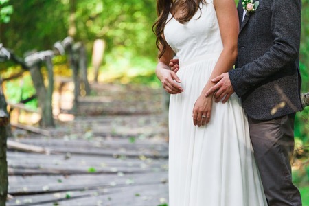 Groom and bride cropped image. Unrecognizable woman in wedding dress with man stand outdoors in summer park, shoot made with copy space. Happy coupleの写真素材