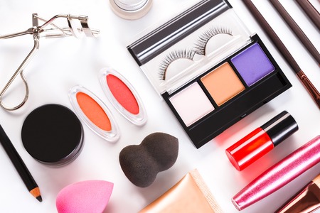 Makeup cosmetics, brushes and other essentials on white background. Top view, flat lay. Multicolored beauty tools and products collection, lipsticks, eyeshadow, blush, sponge, eyelashes and moreの写真素材