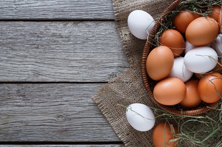 Poultry farm concept. Basket with fresh brown and white eggs on burlap textile at rustic wood...