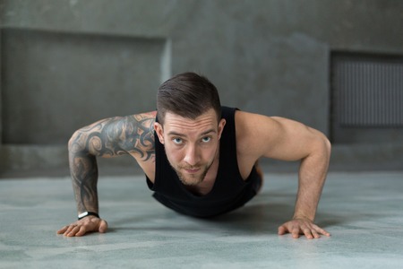 Young man workout in fitness club. Closeup portrait of caucasian guy making plank or push ups exercise, training indoorsの写真素材