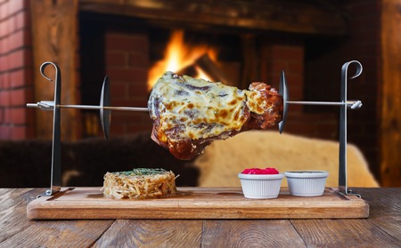 Grill dish in restaurant with fireplace. Grilled roasted pork knuckle on spit with fried sauerkraut cabbage and sauces. Juicy meat meal, german foodの写真素材