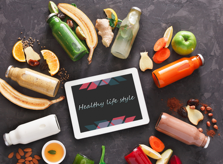 Healthy detox drinks with fruit and vegetable ingredients and tablet with copy space on screen at black background. Glass bottles with smoothie, top view, flat lay. Internet order online conceptの写真素材