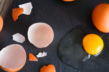 Fresh chicken brown home eggs with cracked eggshell and yolk on rustic slate black background....