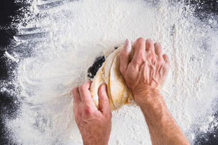 Baking concept. Flour, milk, butter, yeast and eggs carton on rustic wooden table, cooking ingredients. Unrecognizable man's hands top view knead dough on black background. Male bakerの写真素材