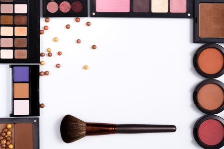 Makeup cosmetics, brush and other essentials frame on white background. Top view, flat lay with copy space. Beauty tools palettes collection, lipstick, eyeshadow, blush, foundation and moreの写真素材