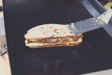 Fresh sandwich on grill. Cookout bbq food. Whole grain bread with roasted onion, meat and vegetables filling closeup. Vendor with spatula cooking street fast food.の写真素材