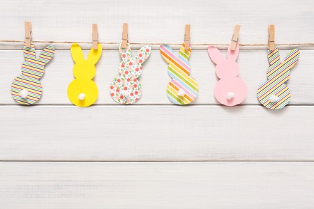 Easter bunny craft paper garland decoration background. DIY holiday handicraft stripe of colorful rabbits. Top view with copy space on white woodの写真素材