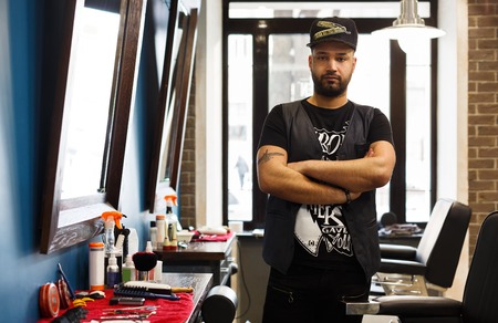 Portrait of successful barber in male barbershop stands with arms crossed. Hair salon service occupation, professional man hairstylist. Lifestyle image of hipster hairdresser with beard and tattooの写真素材