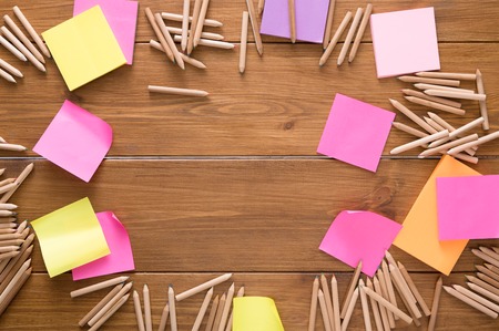 Stationery - top view flat lay shot of many multicolored blank sticky and memo notes and color pencils made round frame on wooden table background, copy space, nobody, objectsの写真素材