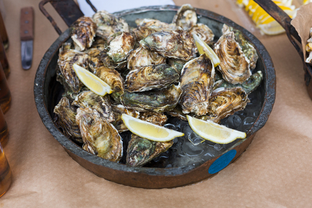 Fresh grilled oysters at grill pan. Seafood delicacy barbecue outdoors. Picnic healthy food, oysters in shells cooked at large metallic pan with lemon slices. Mediterranean cuisineの写真素材