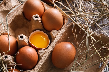 Eggs carton closeup, fresh natural healthy food background. Brown cracked eggs with bright yellow...