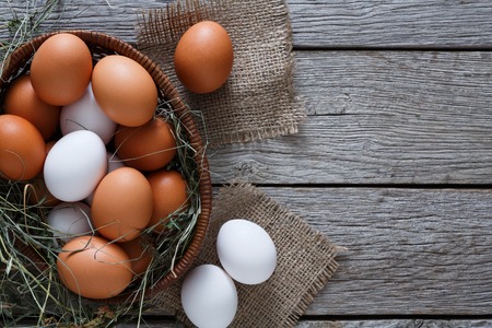 Poultry farm concept. Basket with fresh brown and white eggs on burlap textile at rustic wood...