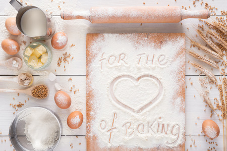 Love baking background. Cooking ingredients for yeast dough and pastry, eggs, butter and board sprinkled with flour, top viewの写真素材