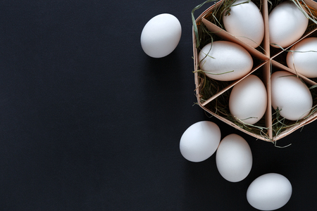 Fresh chicken eggs on black background. White eggs in craft carton pack. Top view with copy space. Rural still life, natural healthy food and organic farming concept.の写真素材