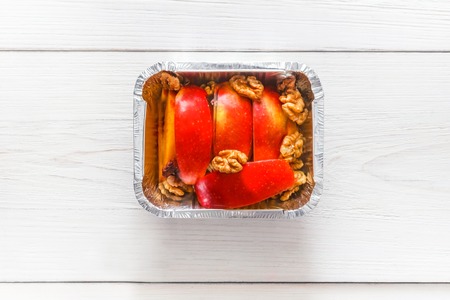 Healthy snack or lunch top view. Natural food in foil box, diet concept. Apple dessert with walnutsの写真素材