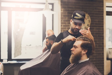 Man getting haircut by hairstylist at barbershop. Stylish barber and clientの写真素材