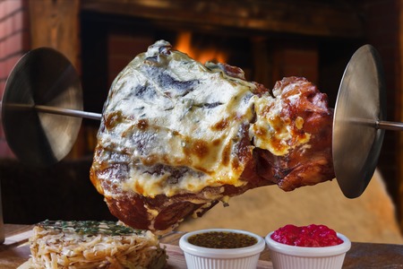 Grill dish in restaurant with fireplace. Grilled roasted pork knuckle closeup on spit with fried sauerkraut cabbage and sauces. Juicy meat meal, german foodの写真素材