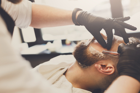 Barber styling beard with razor at barbershop, closeup. Stylish hairdresser in male hair salonの写真素材