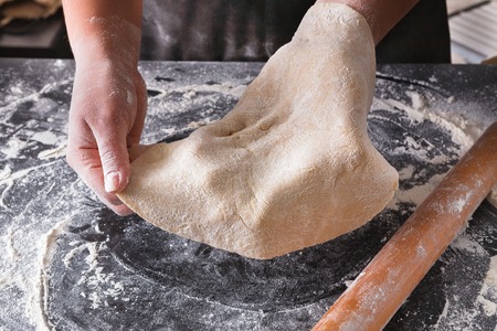 Baking pizza concept. Hands show thin dough on black background. Baker cooking pastry