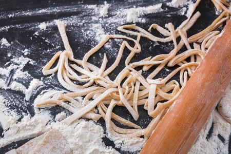 Making homemade noodles on black background, sprinkled wheat flour and raw pasta. Cooking dough