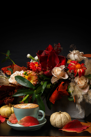 Cappuccino and beautiful flowers bouquet still life. Flower shop composition. Coffee cup, pumpkins on black wood background. Florist art and floral design conceptの写真素材